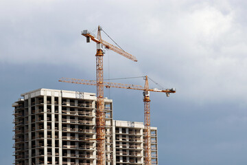 Construction cranes above unfinished residential buildings on storm sky background. Housing...