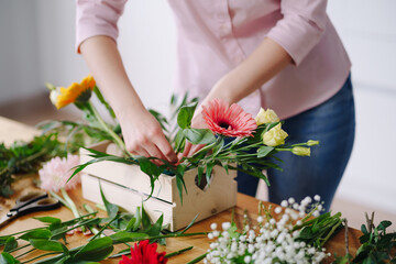 Florist at work: pretty young brunette woman making fashion modern composition of different flowers at home