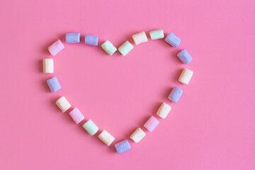 Text Happy and heart shape made by colorful marshmallows on pink background, macro. Fluffy marshmallows texture close up in pastel colors