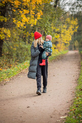 mom and baby on a walk in the autumn park, baby in mom's arms, warm clothes, bright hats