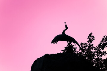The silhouette of a pelican standing over the nest against the pink sunset sky.
