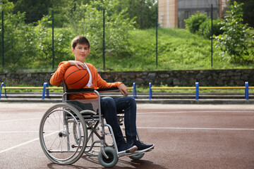 Disabled teenage boy in wheelchair with basketball ball at outdoor court