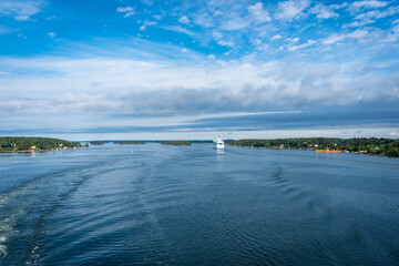 Big cruise ship moving along the coast at sunny summer day. Forest islands of Scandinavia. Beautiful clouds. Panoramic View of Swedish coast from cruise ship passes through islands of archipelago.