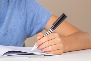 Boy hand holding pen in left hand and writing in a notebook, doing homework. Left Handers Day
