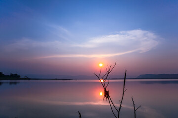 Twilight sunset in the dusk reflection of the water surface, with branches in the foreground,with mountains and the night sky in the background
