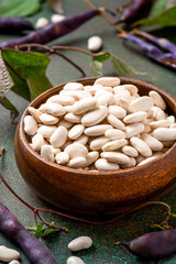 Dry white beans in a wooden bowl on a dark background. Uncooked beans, pod beans, and leaves.