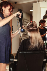 Hairdresser does hairstyle cute young woman in beauty salon