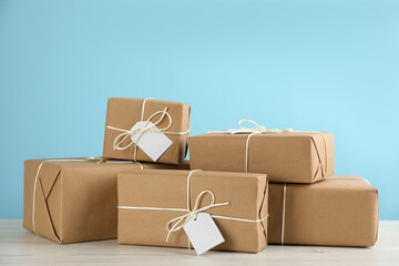 Parcels wrapped in kraft paper with tags on white wooden table against light blue background