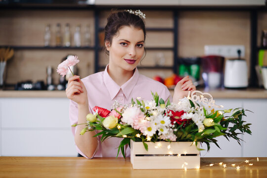 Florist at work: pretty young brunette woman making fashion modern composition of different flowers decorating with led lights at home