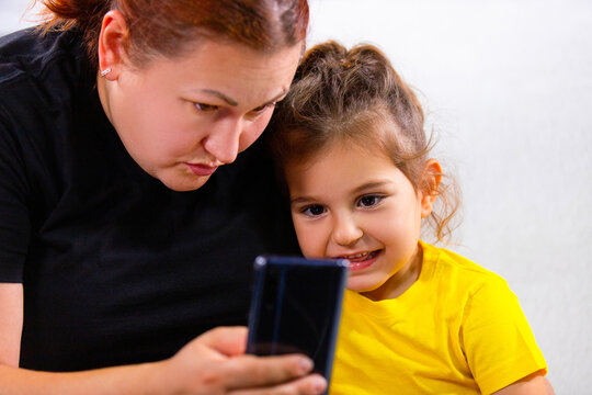 Close up photo of Mom and little girl sitting on the sofa and watching bad news headlines using mobile phone, they are addicted to the phone.