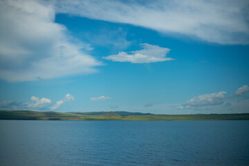 The opposite shore of the azure lake against the blue sky with white clouds.