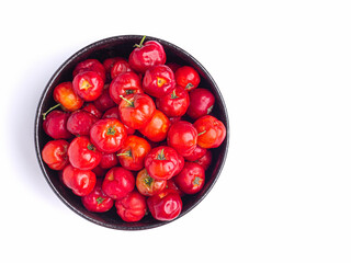 Top view of ripe red acerola cherries fruit in a ceramic bowl isolated on white background. High vitamin C and antioxidant fruits. Close-up photo. Space for text. Concept of healthy fruits