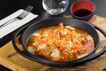 Shrimp casserole with tomatoes and peppers in a black stone pan.
