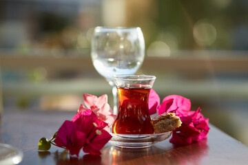 Obraz na płótnie Canvas Turkish delight and traditional glass of turkish tea with bougainvillea flowers. Romantic dinner concept. Relaxing, calming drink Travel Turkey concept. Bright relaxing drink