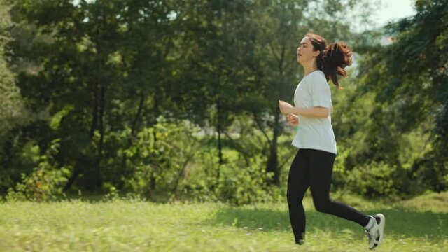 Summer outdoors activity. A young fit woman is jogging in the park, stops because of shortness of breath and continues running. Slow motion.