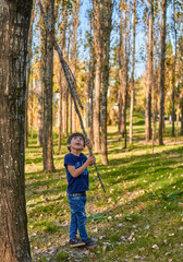 hispanic boy playing alone looking up holding a tree branch in the middle of the forest. fall time. unfocused background. vertical
