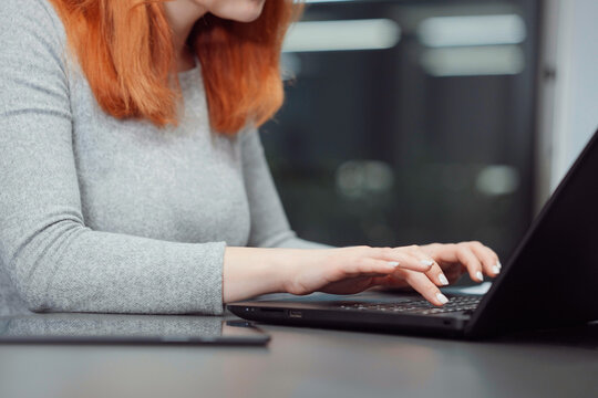 Hands of red-haired woman using laptop and tablet