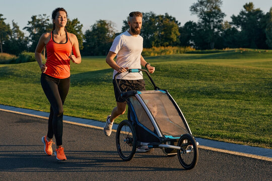 Young family with their child in a jogging stroller during jogging in a park. Active family running