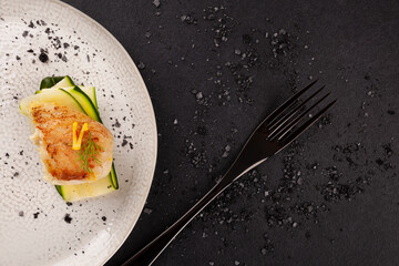 Grilled fish fillet served with zucchini on white plate over black background.
