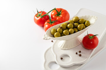 green olives in a decorative dish with red tomatoes on a white background, empty space for text