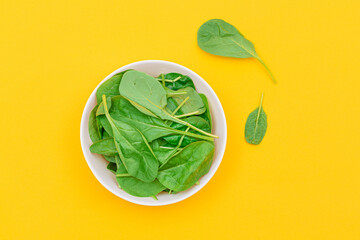 Fresh Baby Spinach Leaves in White Bowl on Yellow Background - Top View. Vegan and Vegetarian Culture. Raw Food, Green Leaves. Healthy Diet