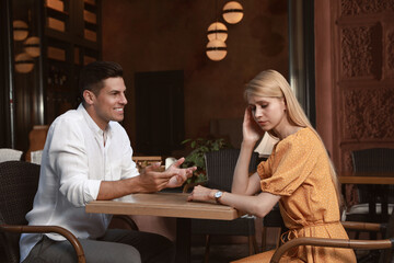 Young woman having boring date with talkative man in outdoor cafe