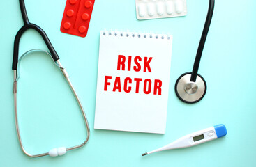 The red text RISK FACTOR is written on a white notepad that lies next to the stethoscope on a blue...
