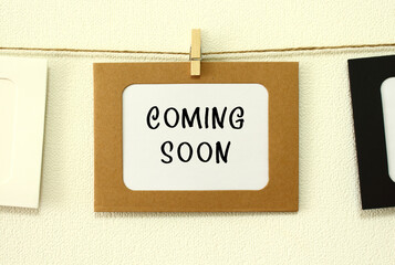 Kraft paper frame hanging on lacing on white wall background. In the frame is written the text COMING SOON.