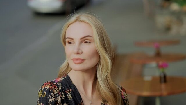 View of pretty blonde woman with wide hazel eyes, city center background. Model posing, touching her hair and face, enjoying springtime. Serious thoughtfull face. Female portrait concept
