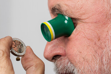 Through his magnifying glass an older, experienced watchmaker looks at a small clockwork.