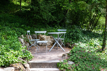 Eine gemütliche Sitzecke im Garten mit Klappstühlen und einem Tisch im Schatten von Bäumen.