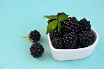 Freshly picked organic blackberries in a white heart shaped bowl on a light blue background.Healthy eating,vegan food or diet concept.
