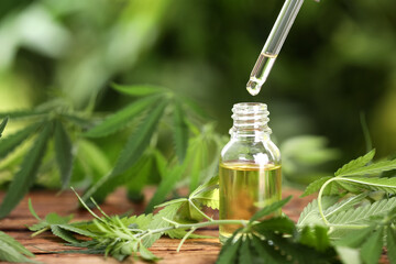 Dripping THC tincture or CBD oil into bottle on wooden table with hemp leaves. Space for text