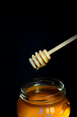 Fototapeta na wymiar honey flows down a spoon into a jar on a black background. High quality photo