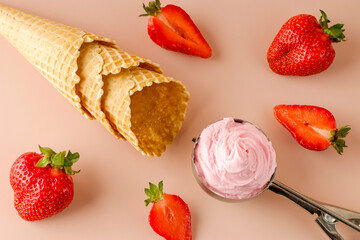 Natural strawberry ice cream in a special spoon. Fresh strawberries and waffle cones on a pink background. Cold summer dessert. Flat lay