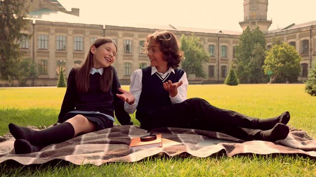 Two glad cheerful kids sit checkered blanket talk