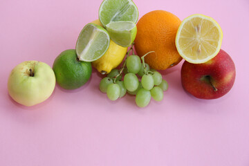 fresh fruit apple, lime, avocado, lemon, orange, grapes on a light pink background