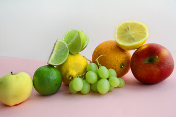 fresh fruit apple, lime, avocado, lemon, orange, grapes on a light pink background
