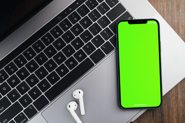 Blank green screen smartphone on wooden background with a computer beside it. Chroma Key.