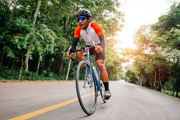 Obraz premium A man ride on bike on the road. Man riding vintage sports bike for evening exercise. A man ride bicycle to breathe in the fresh air in midst of nature, meadow, forest, with evening sun shining through