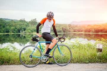 A man ride on bike on the road. Man riding vintage sports bike for evening exercise. A man ride bicycle to breathe in the fresh air in midst of nature, rivers, forest, with evening sun shining through