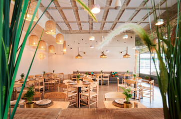 empty rustic design restaurant with wooden furniture seen from a natural frame of plants