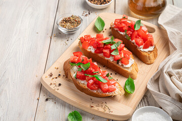 Italian bruschetta with tomatoes, soft cheese and basil on a beige wooden background.