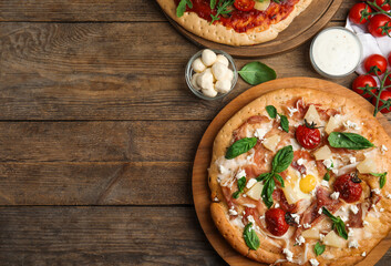 Delicious pita pizzas with prosciutto, pineapple, grilled tomatoes and egg on wooden table, flat lay. Space for text