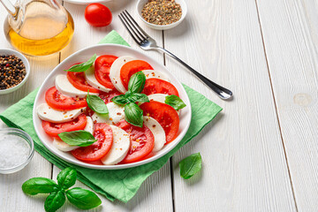 Healthy, Italian caprese salad made of fresh chopped tomatoes, mozzarella cheese and basil on a white, wooden background.