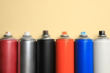 Cans of different spray paints on beige background, flat lay with space for text. Graffiti supplies