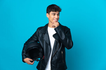 Young man with a motorcycle helmet over isolated blue background looking to the side and smiling