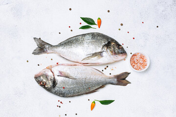 Raw dorado fish with spices and vegetables on light marble table top view.