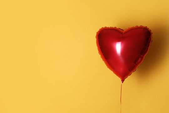 Festive heart shaped balloon on yellow background. Space for text