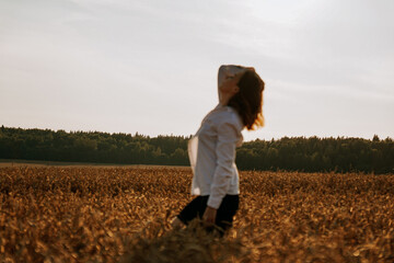 A woman in a wheat field makes flowing movements. The concept of calmness and meditation. Blurred background, focus to foreground